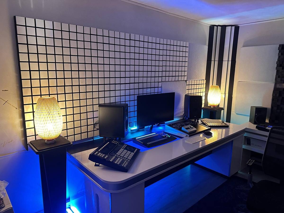 The studio desk: monitors, controllers and acoustic panelling under blue and warm light